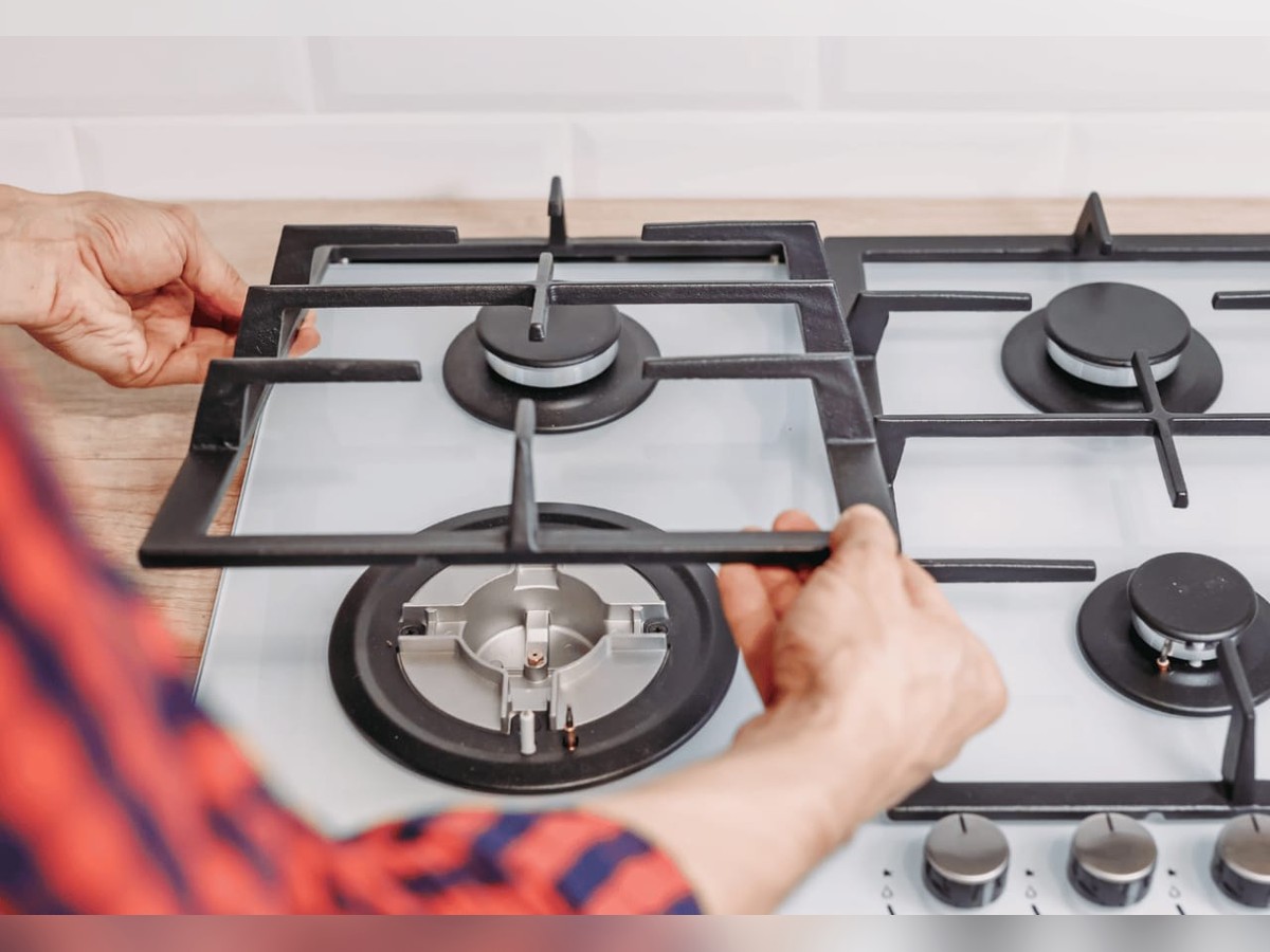 Technician lifting the burner grate off a gas stove to service the burners underneath